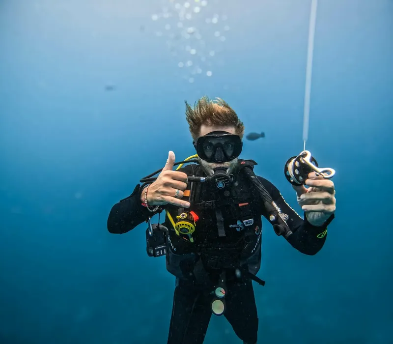 Plongeur souriant avec signe OK, combinaison et équipement complet sous l'eau