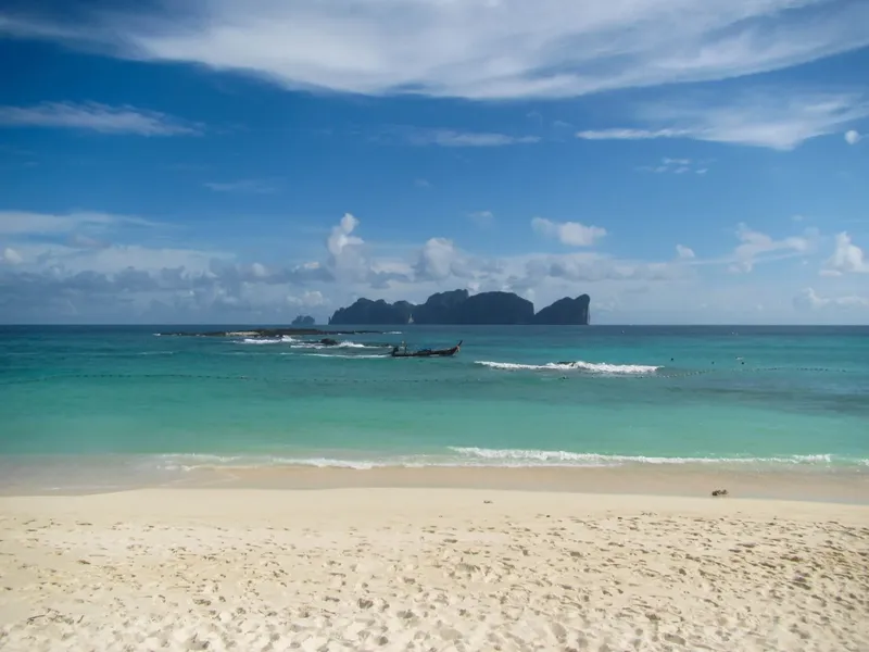 Plage de sable blanc, mer turquoise et îles rocheuses sous ciel bleu