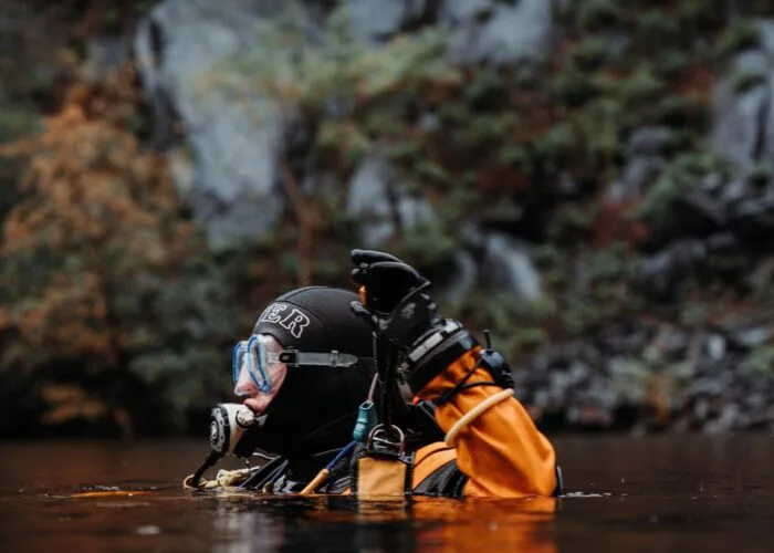 Plongeur en combinaison sèche explore un milieu aquatique rocheux sombre
