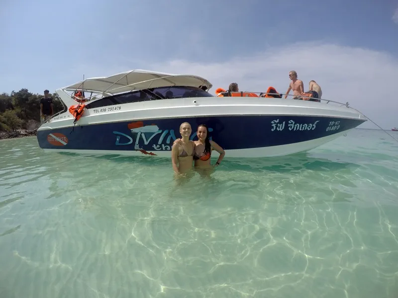 Personnes dans l'eau turquoise devant un bateau de plongée rapide