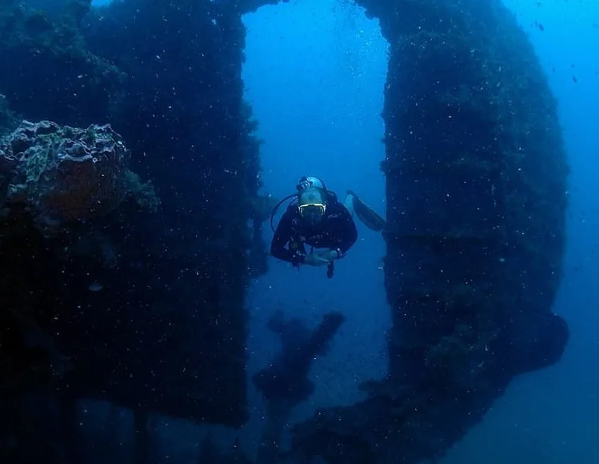 Plongeur explorant une épave sous-marine avec une lumière bleutée