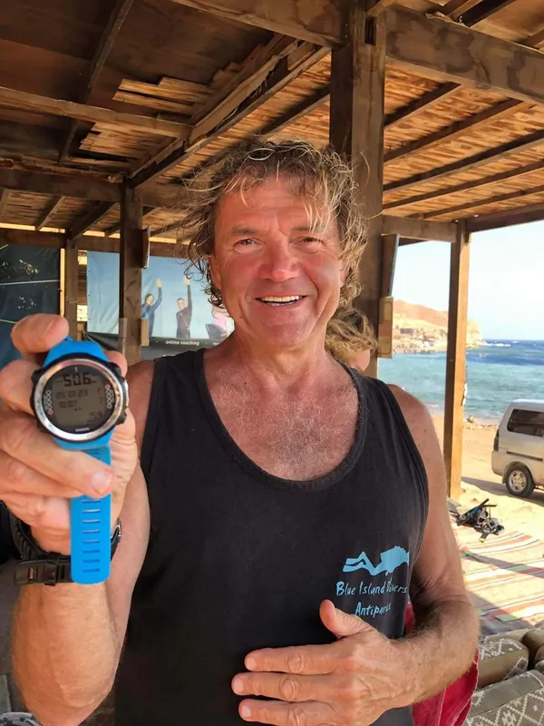 Un homme souriant montre un ordinateur de plongée sur une plage