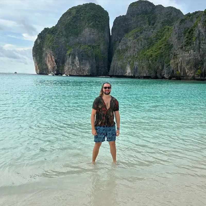 Un homme se tient dans l'eau turquoise devant des falaises