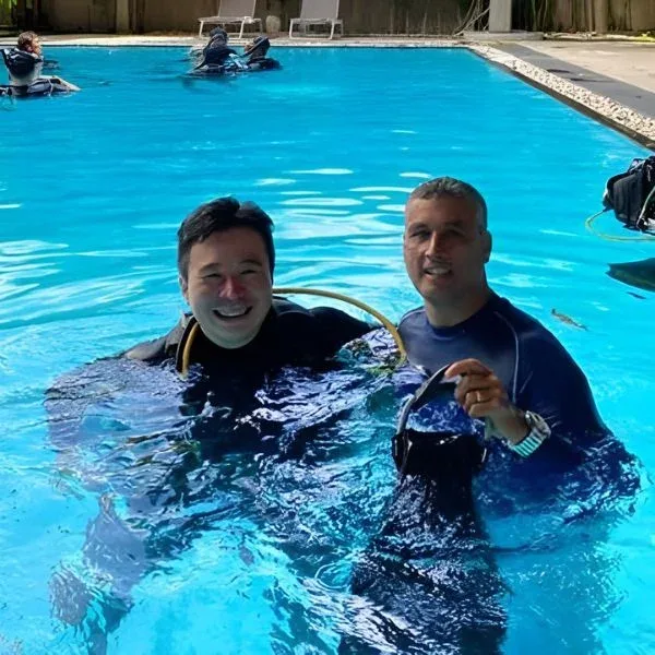 Deux plongeurs souriants en combinaison dans une piscine bleue