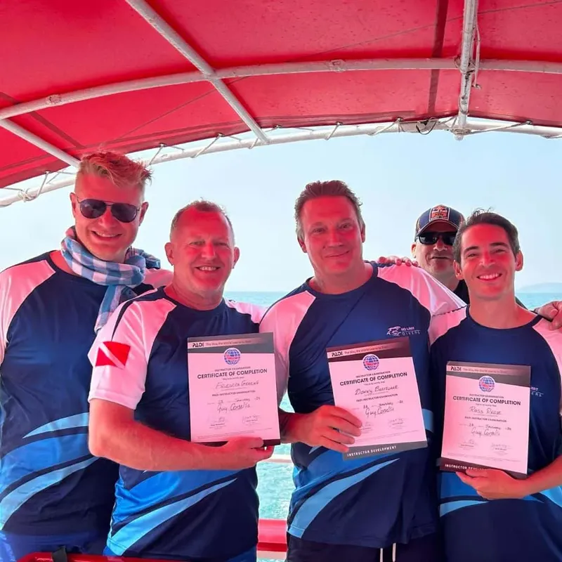 Quatre personnes souriantes présentent des certificats de formation PADI sur un bateau