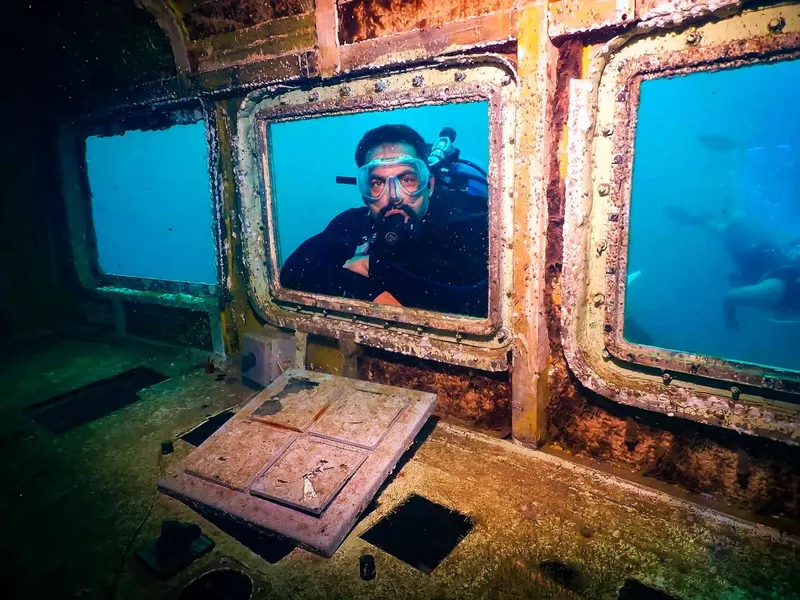 Plongeur regardant à travers une fenêtre d'épave rouillée sous-marine
