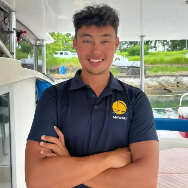 Jeune homme souriant, bras croisés, devant un bateau de plongée