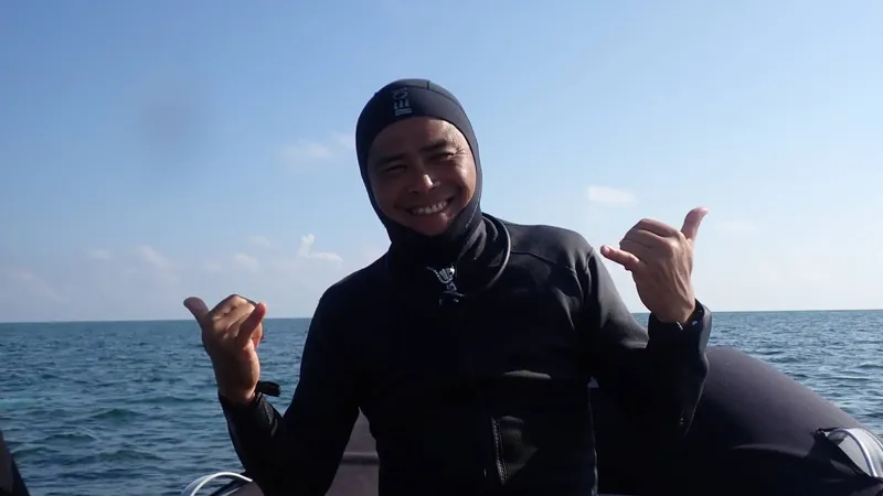 Plongeur souriant en combinaison, faisant le signe de l'océan sur un bateau
