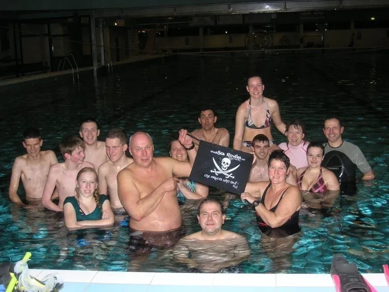 Groupe de personnes souriantes dans une piscine avec un drapeau pirate