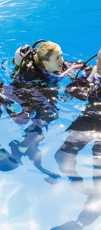 Deux plongeurs en combinaison s'entraînent dans une piscine bleu clair