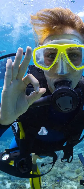 Plongeur souriant avec signe OK, combinaison et masque jaune sous l'eau