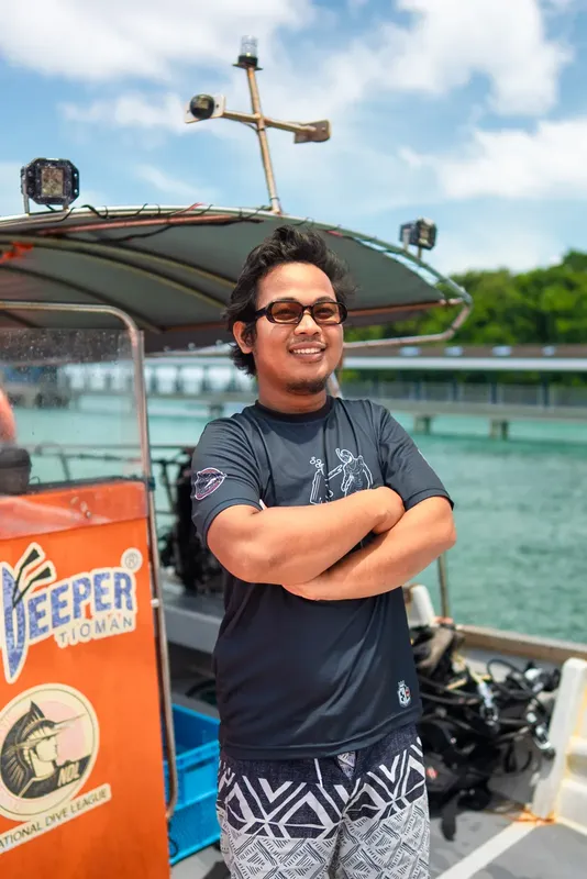 Un homme souriant, les bras croisés, devant un bateau orange et bleu