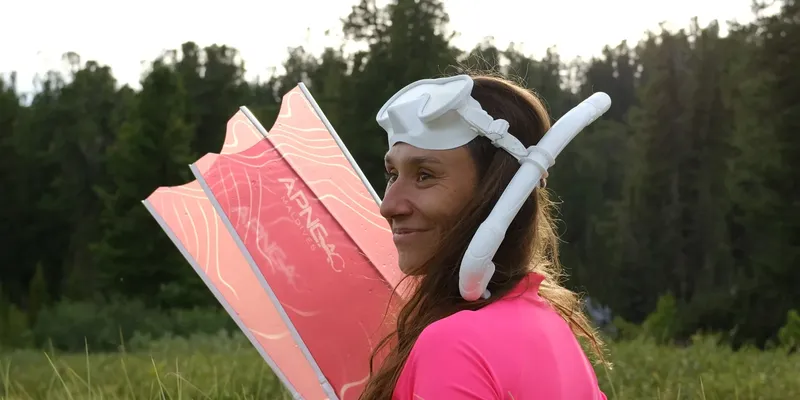 Femme souriante avec masque et tuba tenant une planche rose