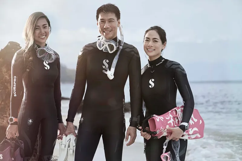 Trois plongeurs souriants en combinaison, masques et détendeurs sur une plage