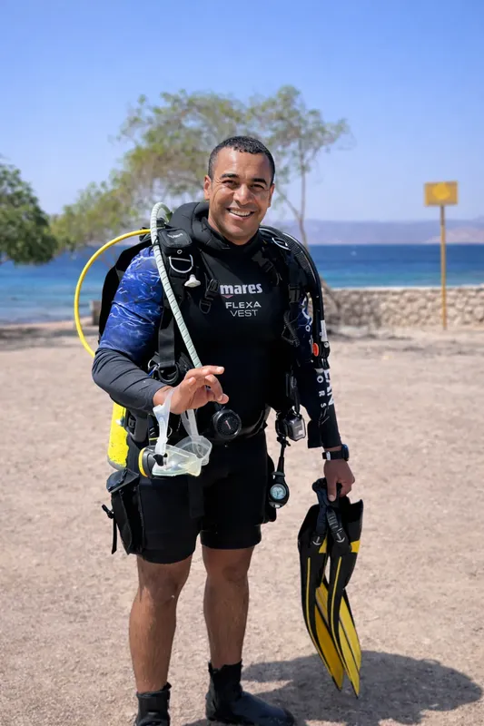 Plongeur souriant, équipé, debout sur une plage de sable clair