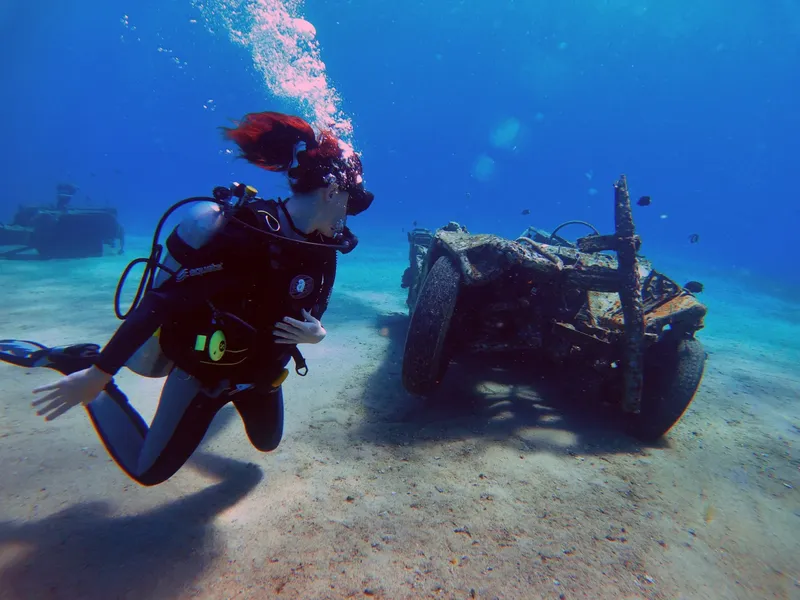 Plongeuse rousse explore une épave sous-marine avec sable clair