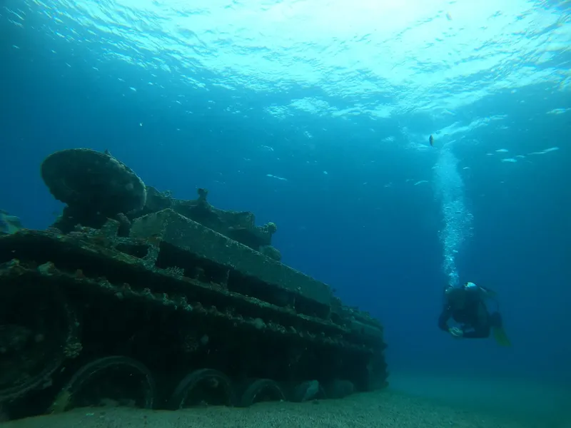 Plongeur explorant un char d'assaut coulé sur fond marin bleu