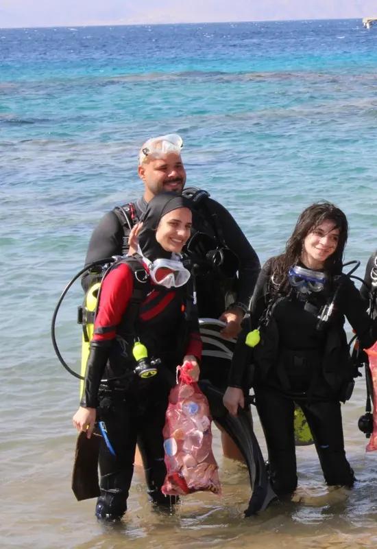 Trois plongeurs souriants sortent de l'eau sur une plage ensoleillée