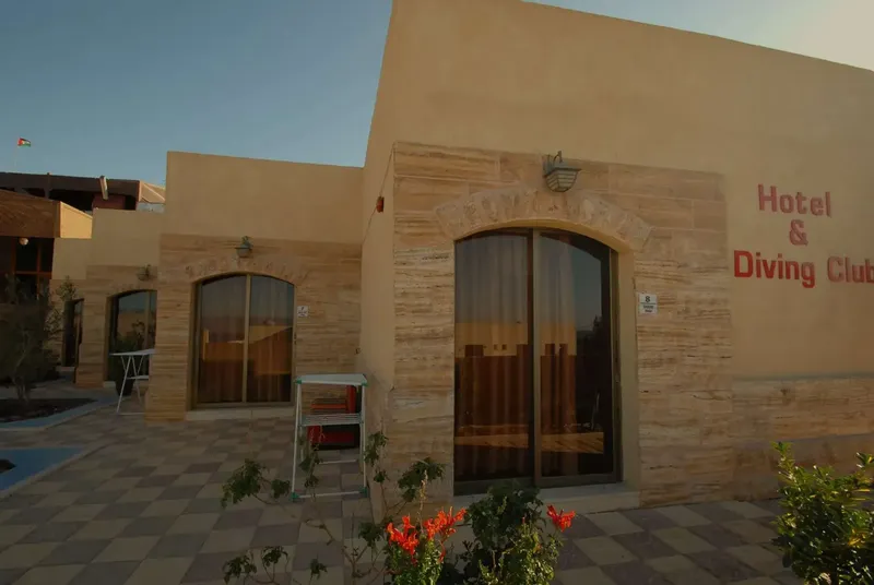 Façade d'un bâtiment beige avec une entrée et des plantes rouges