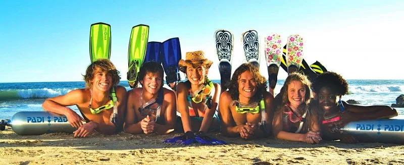 Groupe de jeunes adultes souriants avec du matériel de plongée sur plage