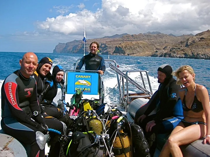 Groupe de plongeurs souriants sur un bateau en mer, équipement visible
