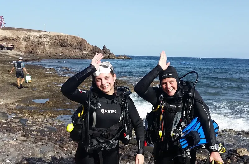 Deux plongeuses souriantes en combinaison sur un rivage rocheux