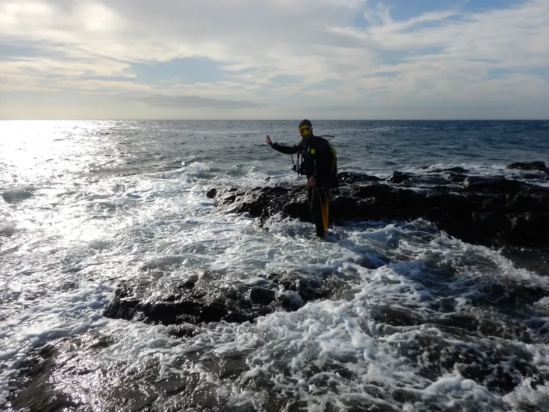 Plongeur en combinaison sortant de l'eau sur des rochers noirs
