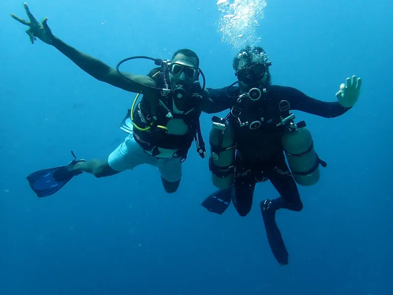 Deux plongeurs souriants nagent ensemble dans une eau bleue claire