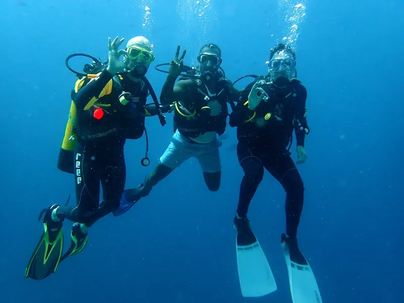 Quatre plongeurs souriants font des signes de paix sous l'eau