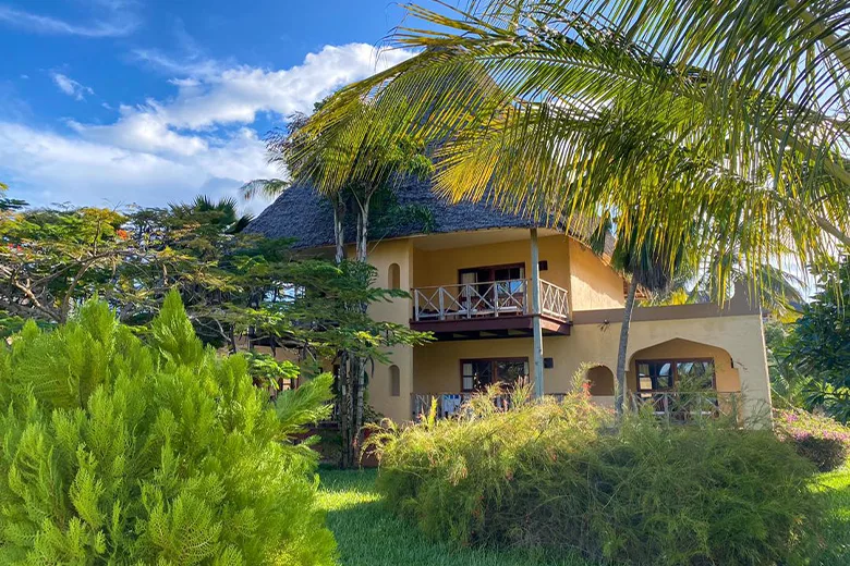 Bâtiment jaune avec balcon, végétation tropicale et ciel bleu nuageux