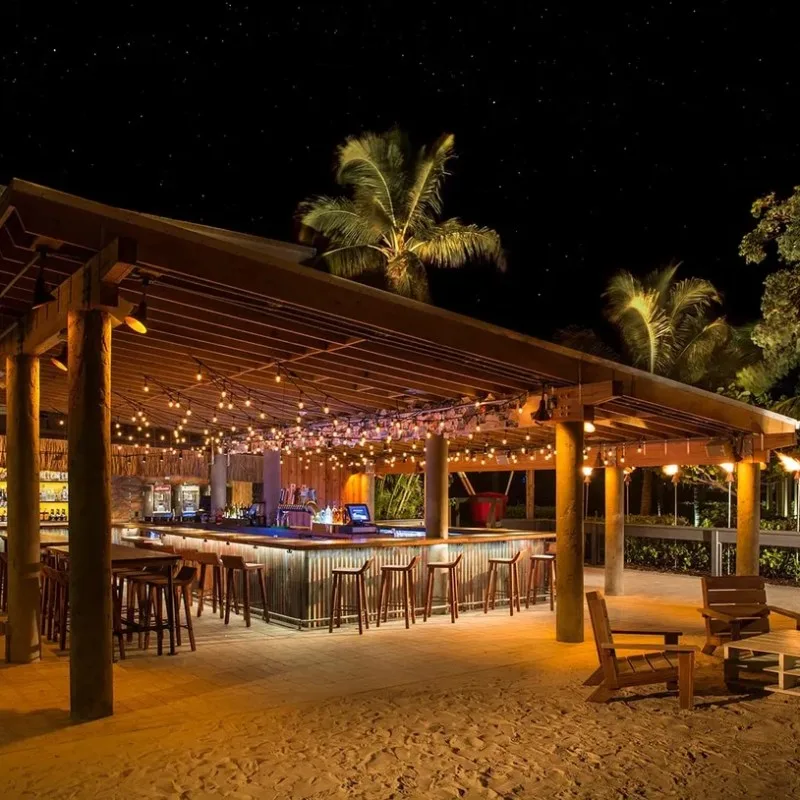 Bar extérieur éclairé la nuit avec des clients et des palmiers