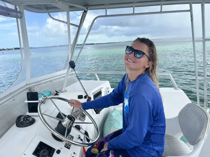 Femme souriante aux lunettes de soleil tient le volant d'un bateau