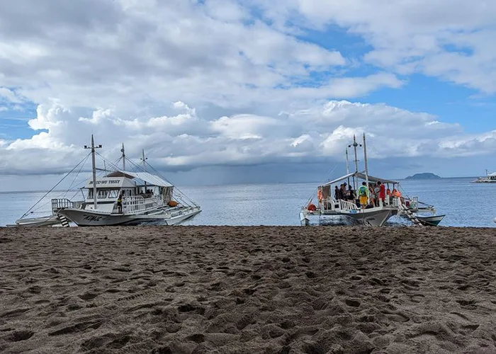Plage de sable noir avec deux bateaux de plongée et des personnes