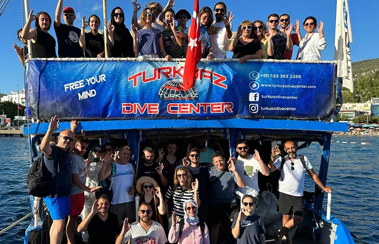 Groupe de plongeurs souriants sur un bateau avec une bannière publicitaire