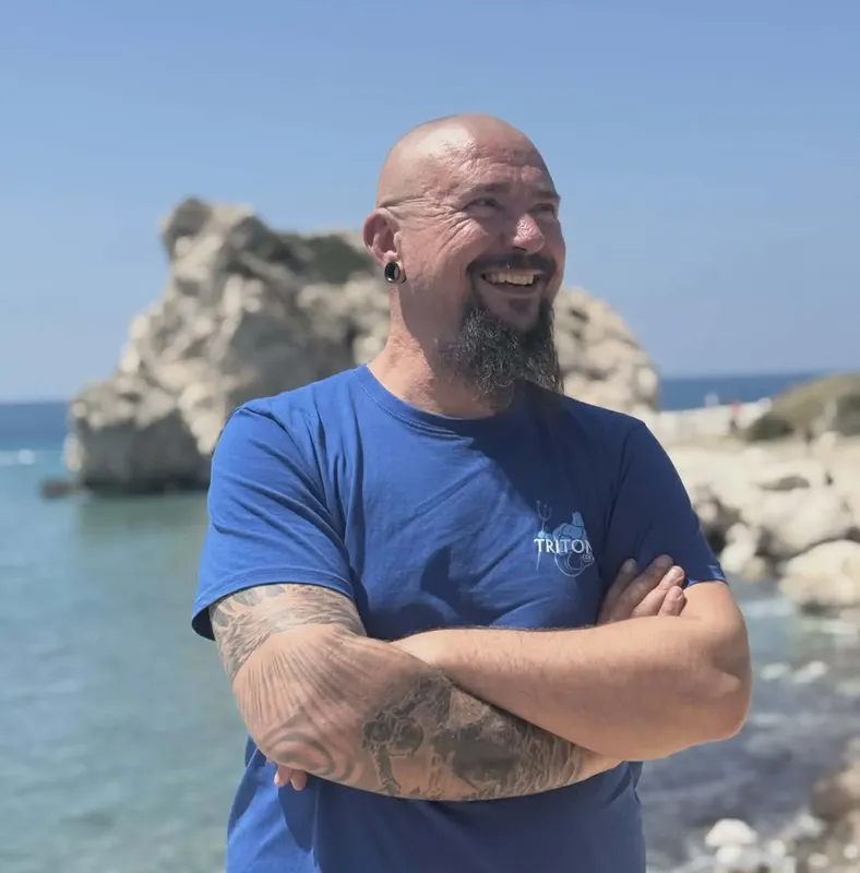 Homme souriant avec tatouages, paysage marin rocheux en arrière-plan