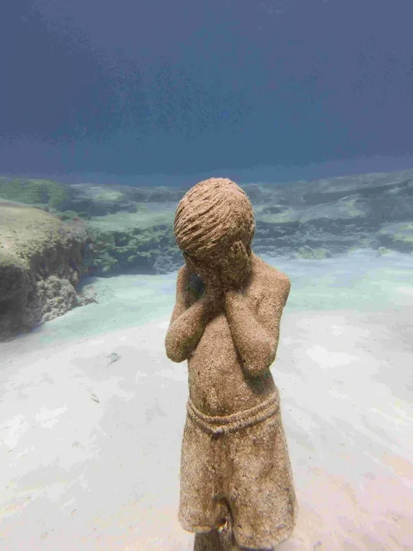 Statue d'enfant recouverte d'algues, immergée dans une eau turquoise claire