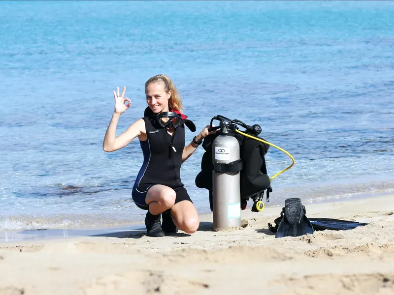 Plongeuse souriante en combinaison et gilet, avec bouteille sur plage