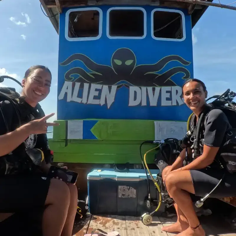 Deux plongeuses souriantes devant une enseigne colorée sur le quai