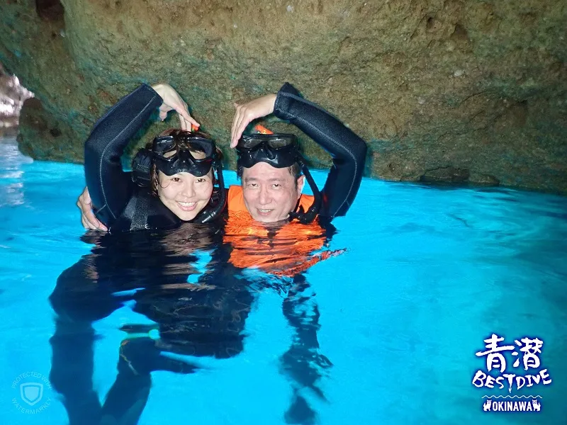 Deux plongeurs souriants avec masque et gilet dans l'eau turquoise