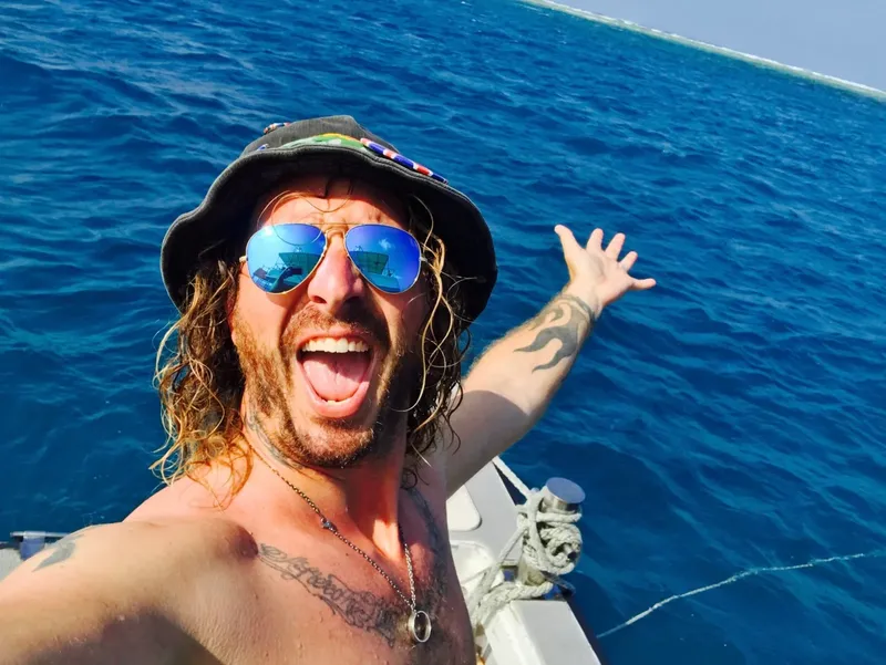 Homme souriant sur un bateau en mer, lunettes de soleil et chapeau