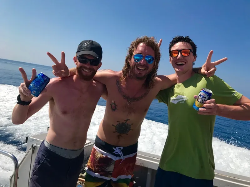 Trois hommes souriants font des signes de la main sur un bateau