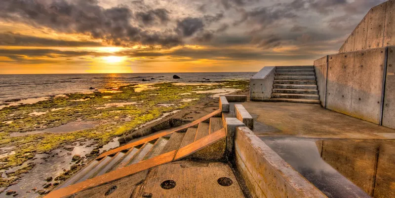 Escaliers en béton donnant sur une plage rocheuse au coucher du soleil