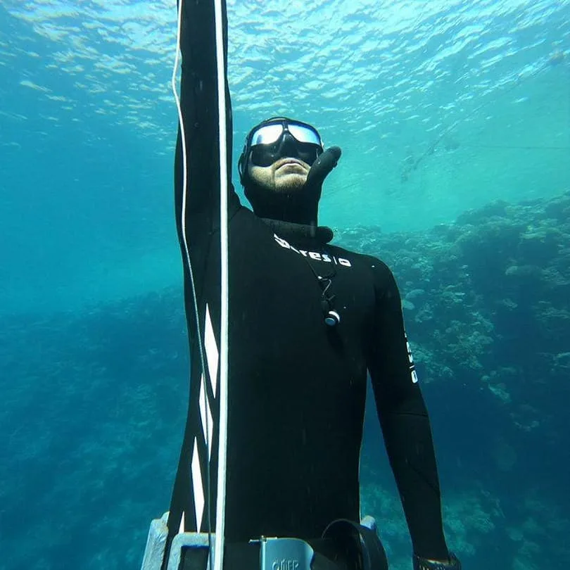 Plongeur en combinaison noire, regardant vers le haut dans l'eau bleue