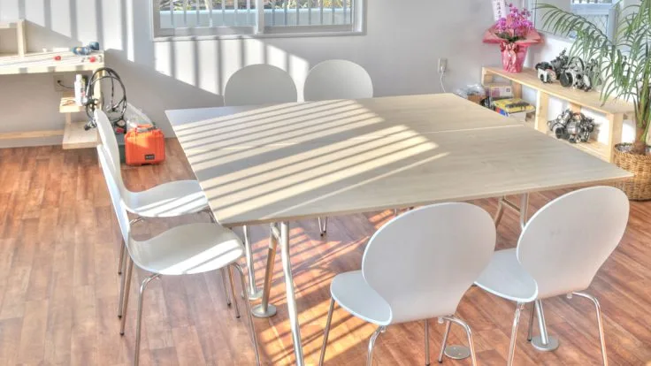 Salle lumineuse avec table, chaises blanches et étagères décoratives