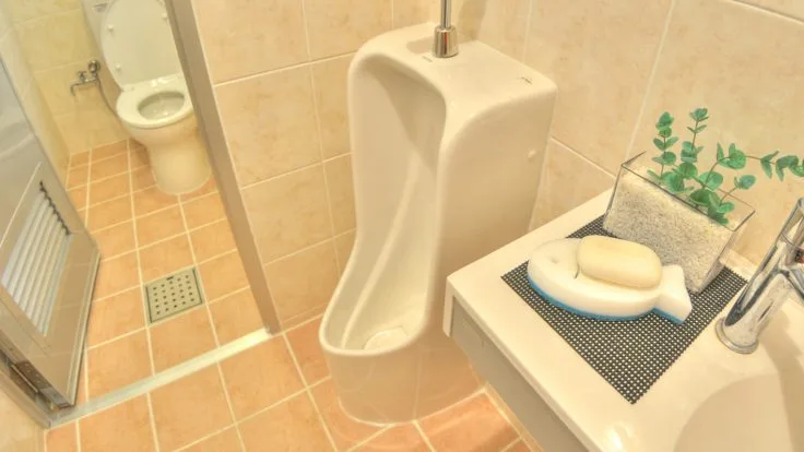 Toilettes publiques avec urinoir blanc et carrelage beige clair