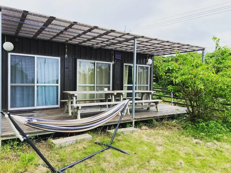 Bâtiment noir avec terrasse en bois, hamac et végétation environnante