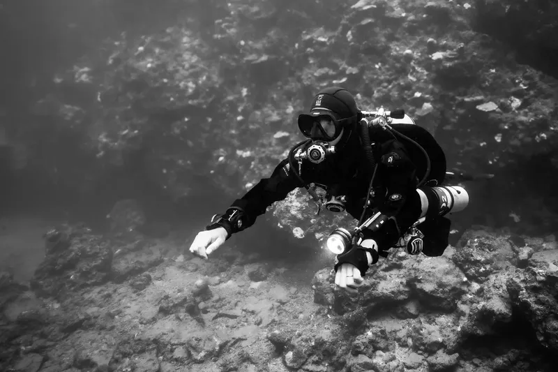Plongeur en combinaison noire explore un fond rocheux sous-marin