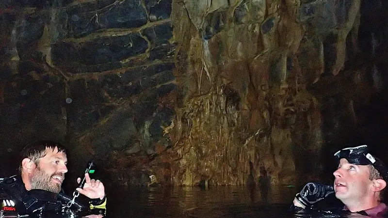 Deux plongeurs explorent une grotte sous-marine, éclairés par leurs lampes