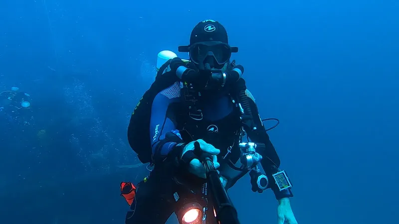 Plongeur équipé en combinaison, masque et détendeur sous l'eau bleue