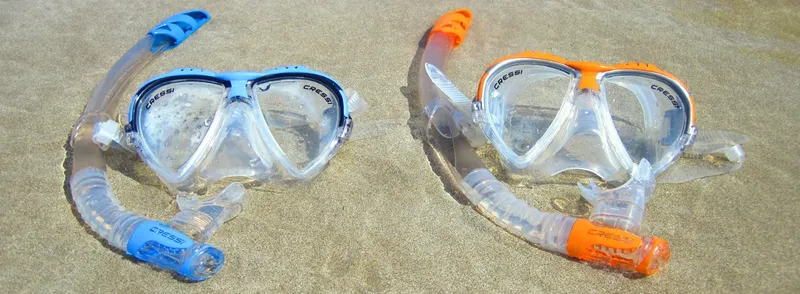 Deux masques et snorkels de plongée colorés sur du sable fin
